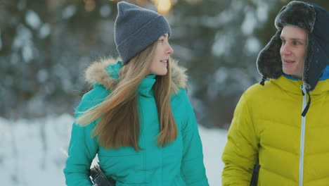 Side-view-portrait-of-active-young-couple-enjoying-skiing-in-beautiful-winter-forest,-focus-on-unrecognizable-woman-holding-ski-poles,-copy-space